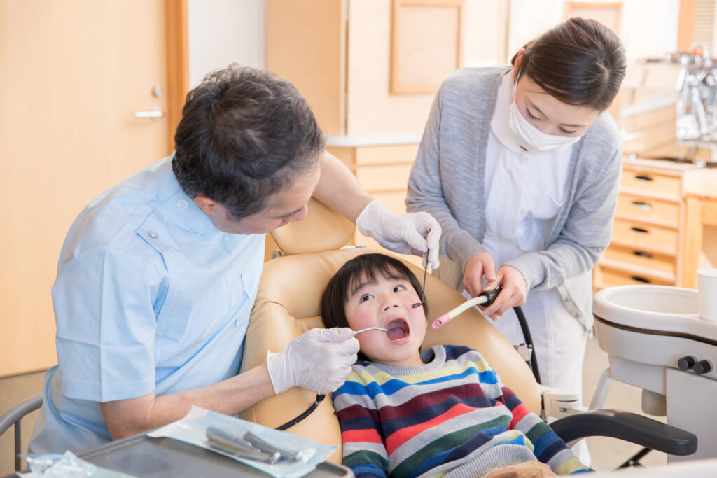 歯医者で歯科治療を受ける男の子と男性医師と女性衛生士
