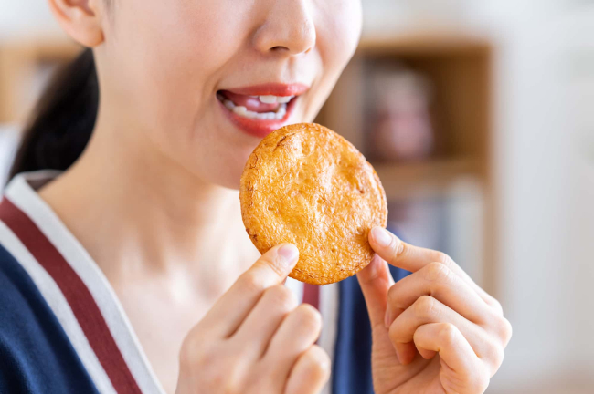 矯正治療中にワイヤーやブラケットが外れる原因となる固い煎餅を食べる女性