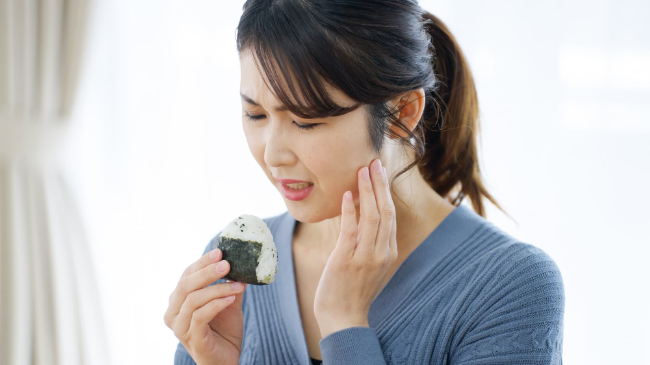 おにぎりを食べようとしているのに口が開きにくくて顔をしかめる女性